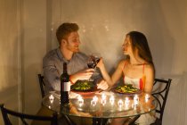 Casal à mesa cara a cara desfrutando de refeição à luz das velas, fazendo um brinde, sorrindo — Fotografia de Stock
