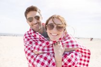 Couple contemporain passer un bon moment sur la plage enveloppé dans une couverture de plage — Photo de stock