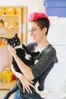 Young woman with pink carrying wide-eyed cat in kitchen — Stock Photo
