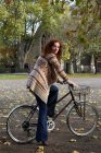 Woman standing on bicycle in park — Stock Photo