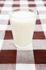 Glass full of milk on checkered tablecloth — Stock Photo