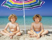 Twin boys under a sun umbrella — Stock Photo