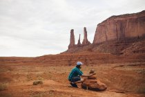 Junger Mann kauert, um auf aufgeschichtete Felsen, Monument Valley, arizona, USA zu schauen — Stockfoto