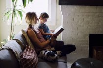 Donna sul divano con la figlia del bambino che legge il libro di favole — Foto stock