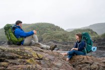 Jeune couple avec sac à dos, assis sur des rochers, Constant Bay, Charleston, Île du Sud, Nouvelle-Zélande — Photo de stock
