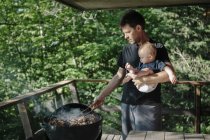 Father holding young son while turning food on barbecue — Stock Photo