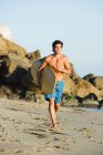 Молодой человек бегает по пляжу с доской для серфинга — стоковое фото