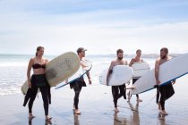 Group of male and female surfer friends walking away from sea with surf boards — Stock Photo