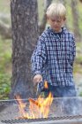 Boy barbecuing sausage on flaming grill in forest, Sedona, Arizona, USA — Stock Photo