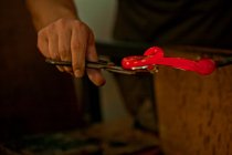 Imagem cortada de pessoa segurando vidro quente vermelho na fábrica de vidro — Fotografia de Stock