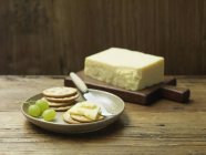 Mature cheddar cheese with water biscuits and grapes on wood — Stock Photo