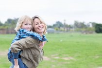 Mother carrying son piggyback outdoors — Stock Photo