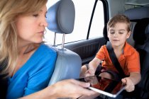 Mãe passando tablet digital para filho no banco de trás do carro — Fotografia de Stock