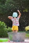 Visão traseira da menina em pé no banho de bolhas no jardim espirrando bolhas de sabão — Fotografia de Stock