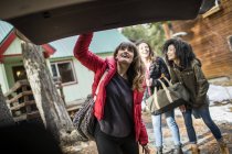 Друзья стоят возле хижины, молодая женщина закрывает багажник машины — стоковое фото