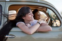 Mujeres jóvenes viajando en coche en viaje por carretera, sonriendo - foto de stock
