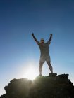 Rear view of man standing on top of rock with arms raised — Stock Photo
