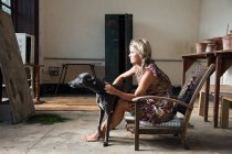 Mujer joven sentada en silla con perro - foto de stock