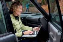 Ältere Frau benutzt Laptop im Auto — Stockfoto