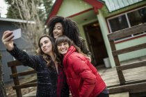 Drei Freunde, die neben der Kabine stehen, Selfie machen, Smartphone benutzen — Stockfoto