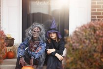 Amigos vestidos de bruja y zombi, sentados en el escalón delantero de casa - foto de stock