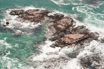 Rocas con olas de surf en agua de mar azul - foto de stock