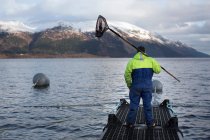Vista posteriore del lavoratore presso l'allevamento di salmoni nel lago rurale — Foto stock