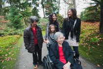 Семья из нескольких поколений толкает пожилую женщину в инвалидном кресле — стоковое фото