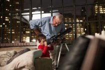 Grandfather teaching grandson to use telescope at home — Stock Photo