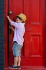 Хлопчик відкриває червоні вхідні двері — стокове фото
