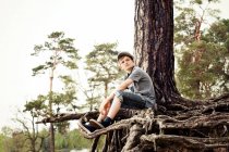 Menino sentado em raízes de tronco de árvore — Fotografia de Stock