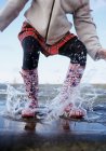 Cropped image of woman in rubber boots jumping in water — Stock Photo