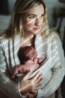 Portrait de femme adulte berçant bébé fille nouveau-né enveloppé dans un cardigan — Photo de stock