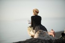 Frau liegt auf Treibholz und blickt aufs Meer — Stockfoto