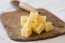 Cubed cheese with knife on wooden cutting board — Stock Photo