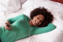 Femme écoutant des écouteurs sur le lit — Photo de stock