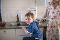Niño en fregadero de cocina mirando por encima del hombro - foto de stock