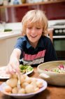 Kleiner Junge am Esstisch der Familie hilft sich mit Kartoffeln — Stockfoto