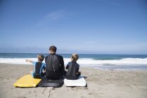 Vista posteriore dell'uomo e due figli seduti su bodyboard che puntano, Laguna Beach, California, USA — Foto stock