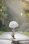 Barefoot girl holding up umbrella and walking through puddles on street — Stock Photo