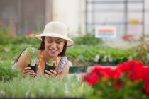 Молодая женщина смотрит на растения в центре сада, улыбаясь — стоковое фото
