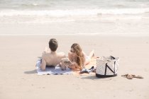 Сучасна пара добре відпочиває на пляжі читаючи і засмагаючи на пляжних рушниках — стокове фото