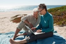 Couple d'âge mûr utilisant un ordinateur portable à la plage — Photo de stock
