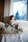 Young girl sitting on bed looking through window — Stock Photo
