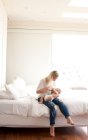 Mulher adulta média sentada na cama amamentando bebê filho — Fotografia de Stock