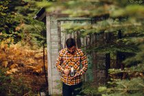 Young man standing near cabin in forest, taking photograph with camera, near Shaver Lake, California, USA — Stock Photo
