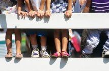 Cropped shot of children leaning against fence in sunlight — Stock Photo
