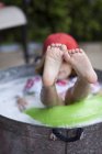 Girl sitting in bubble bath in garden with feet sticking out — Stock Photo