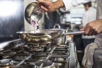 Chef derramando cebolas vermelhas fatiadas em panela no fogão, close-up — Fotografia de Stock