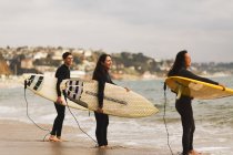 Três amigos de pé no mar, segurando pranchas de surf, se preparando para surfar — Fotografia de Stock